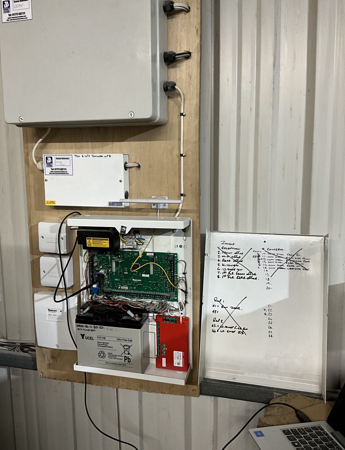 Open alarm panel showing circuit board and battery — J4 Security Systems service engineer